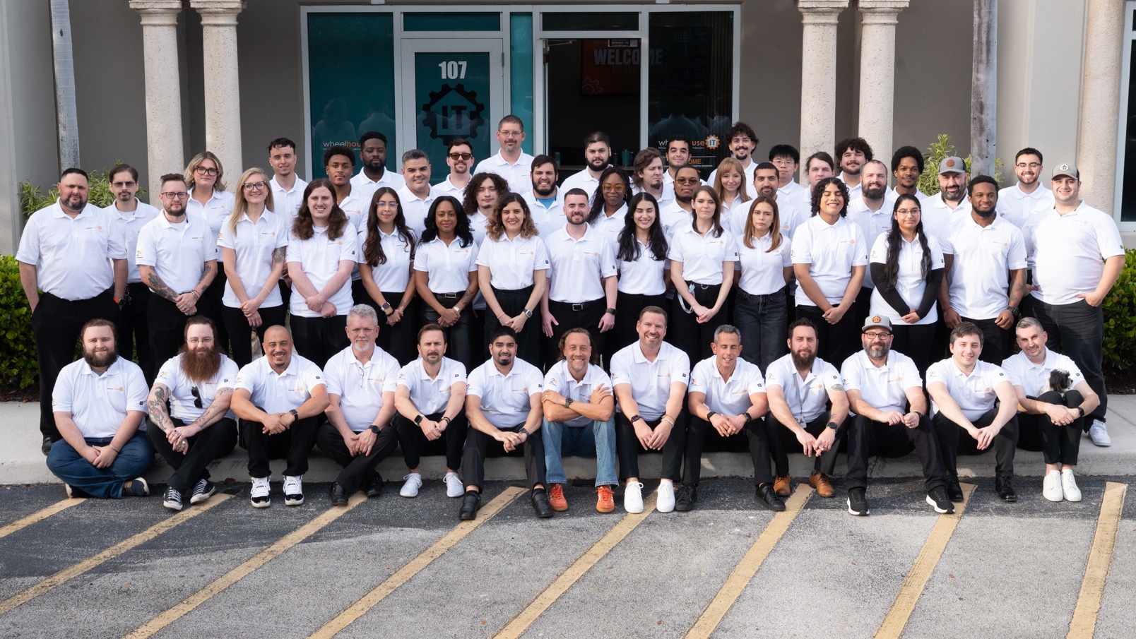 diverse team wearing white shirts poses outside modern building for group photo.