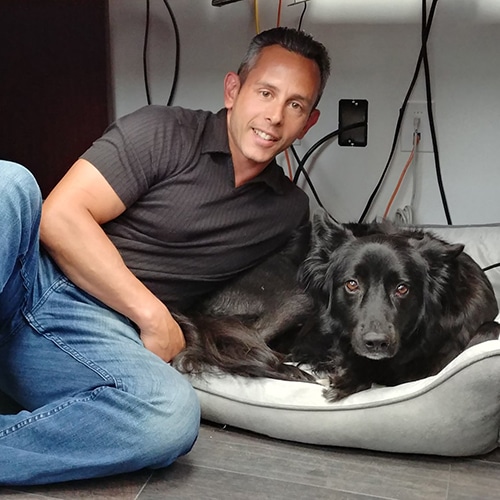 man sitting with black dog in cozy indoor setting, showing companionship and comfort.