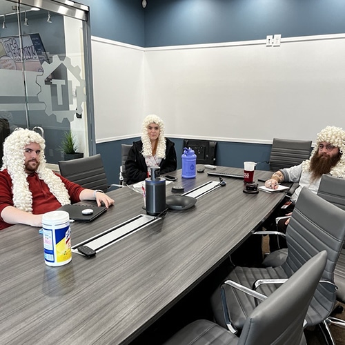 modern conference room with individuals in white wigs, blending humor and professionalism in workspace.