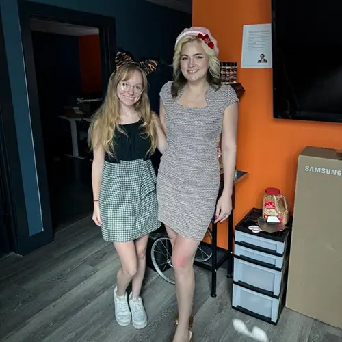 two friends in stylish outfits posing in a modern indoor setting.