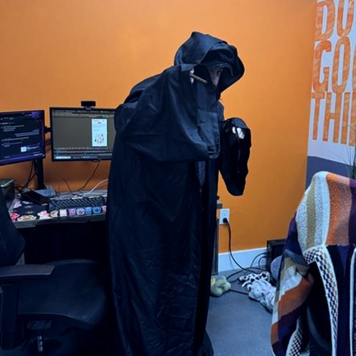 person in dramatic black cloak in modern office workspace with vibrant orange wall.