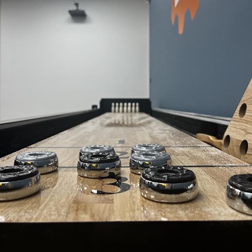 modern shuffleboard table with wooden pucks, pins, and blue wall background.